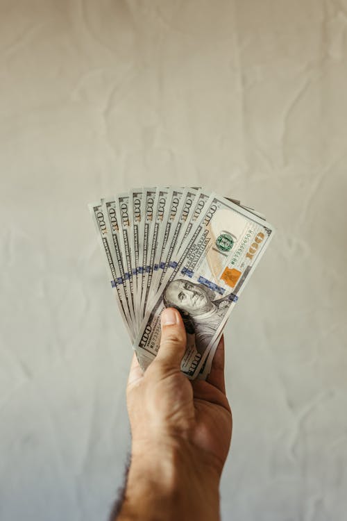 A person holding a fan of 100 US dollar banknotes