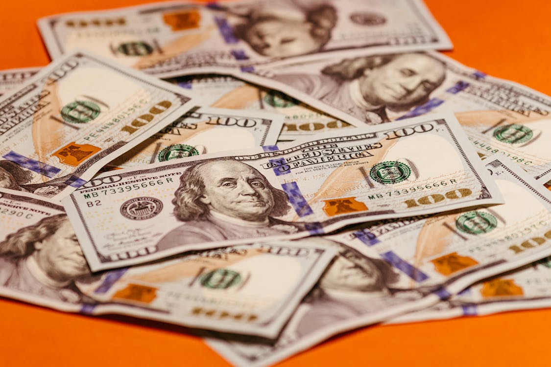 An image of 100 US dollar banknotes on an orange surface