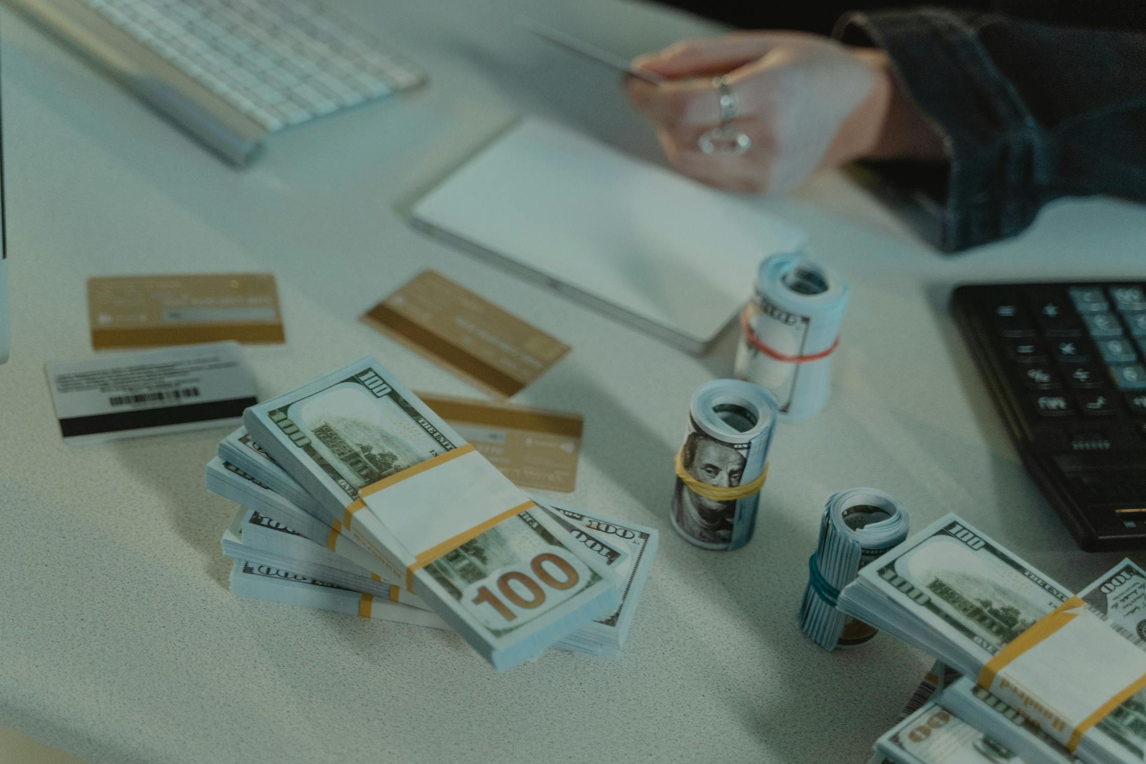 Bundles and rolls of US 100-dollar banknotes on a table along with credit cards and calculator