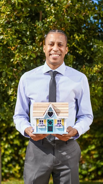 A real estate investor holding a miniature wooden house