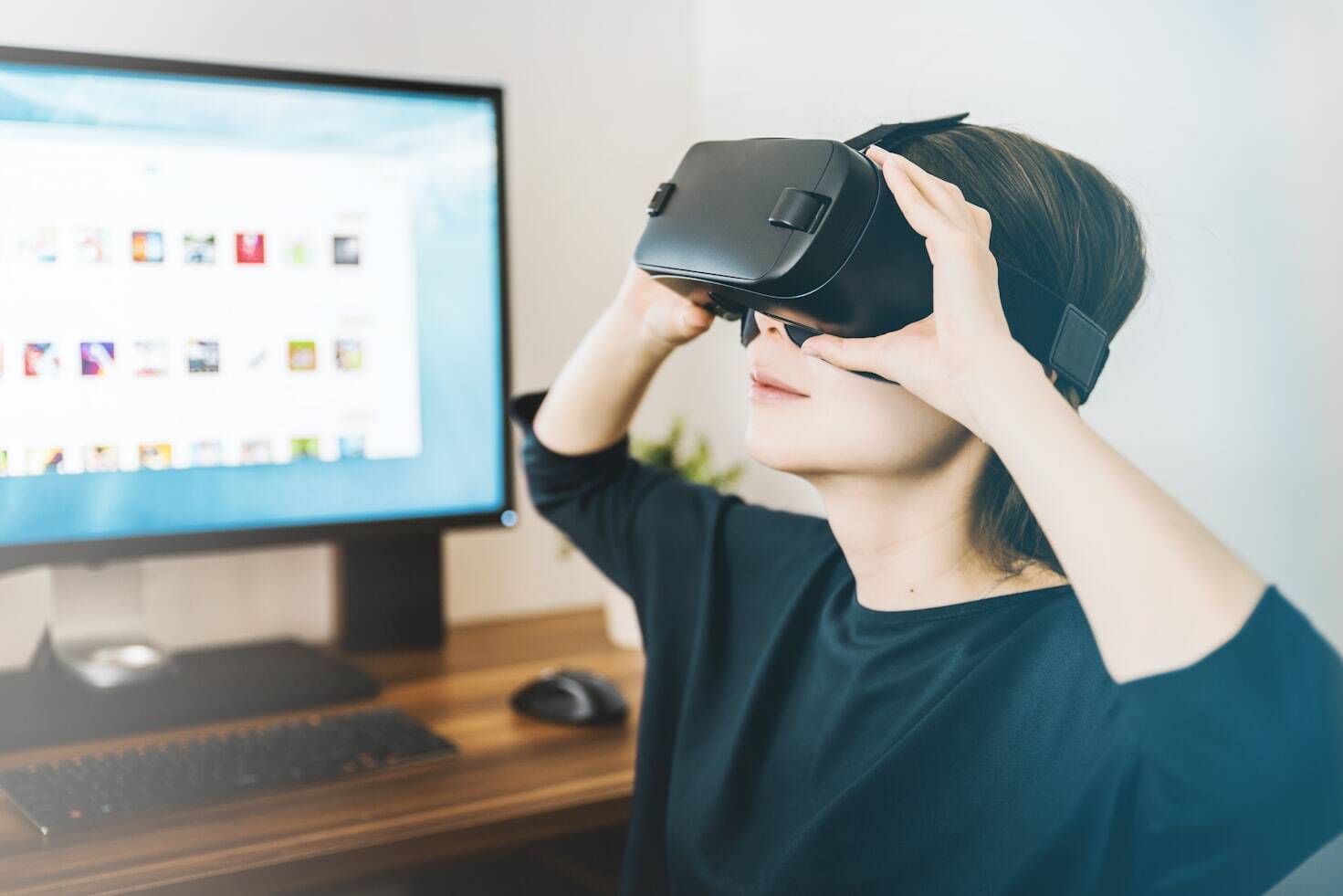 A woman wearing a VR set with a computer in the background