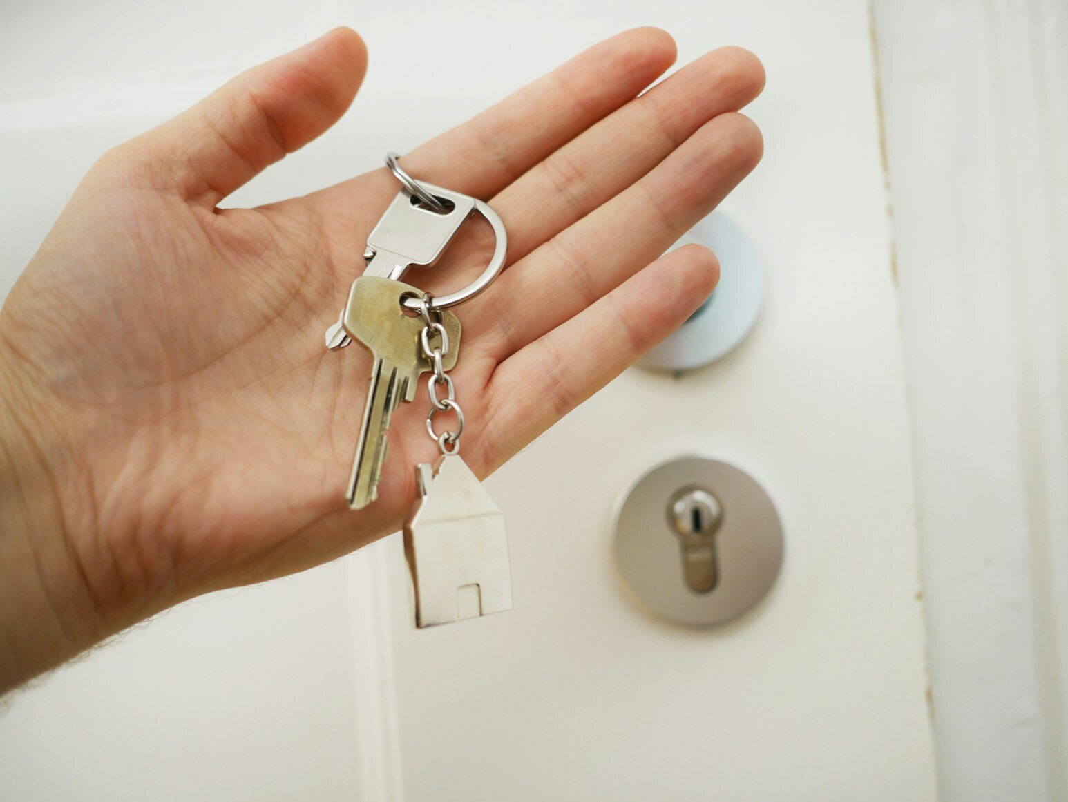 A closeup of a person holding a key with a home keychain in front of a door