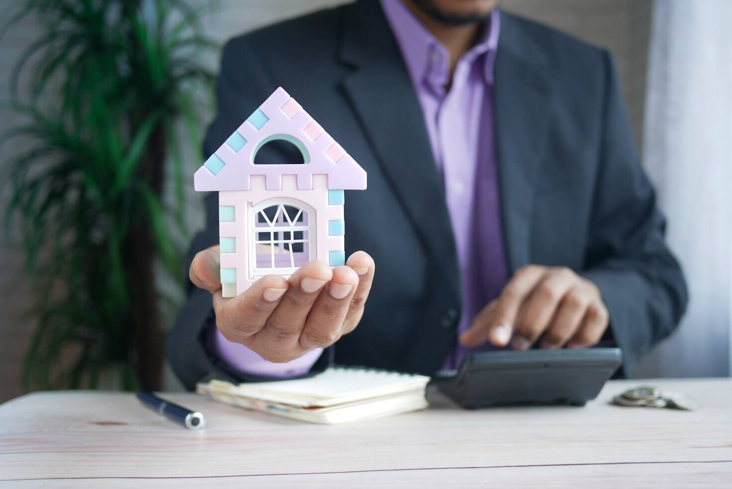 A closeup of a person in a suit holding a miniature house