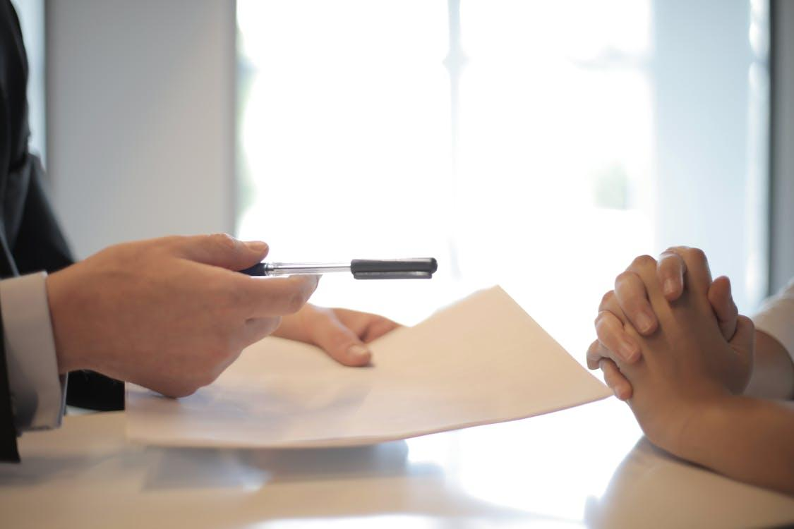 a person handing over a document and pen