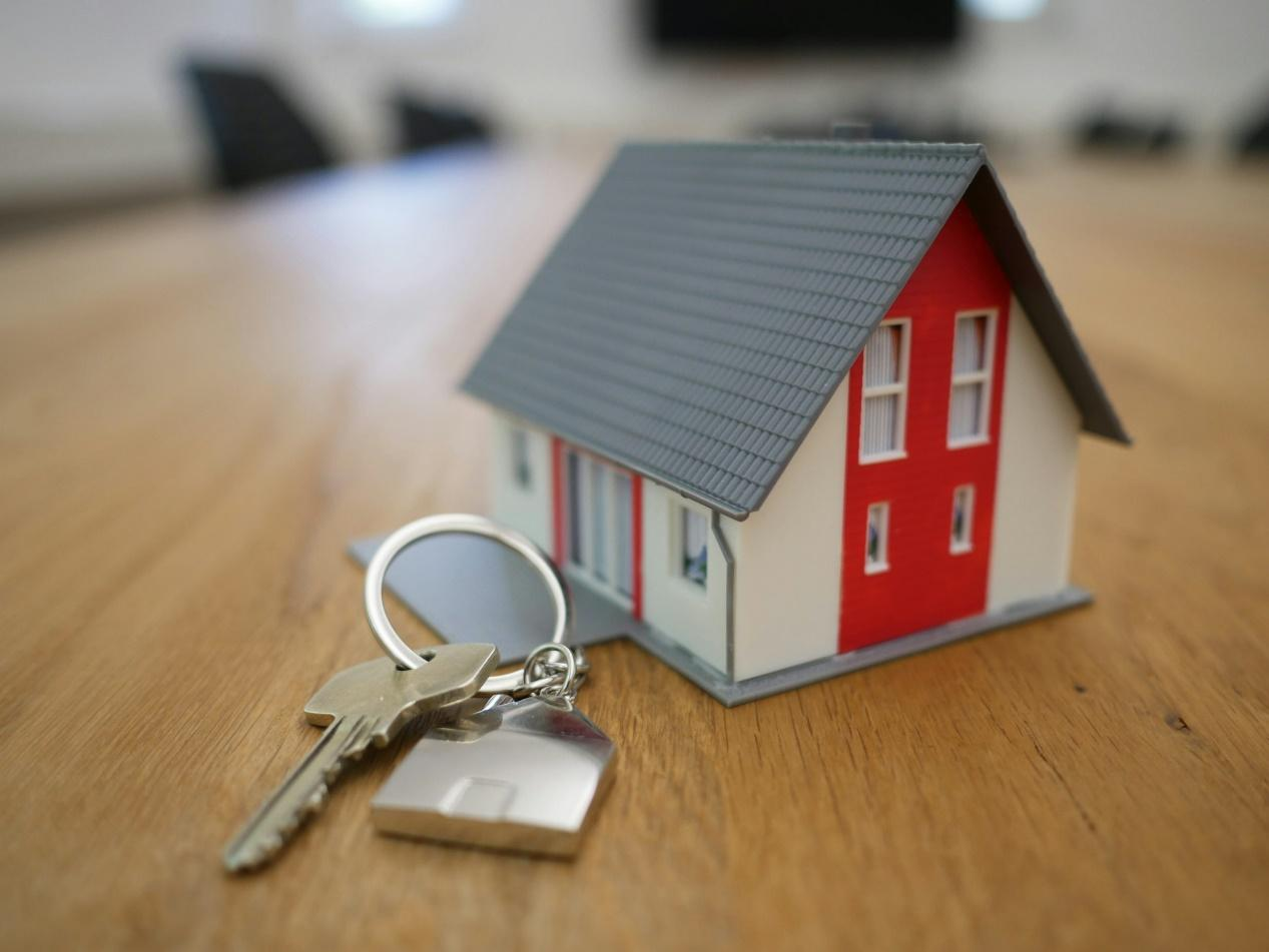 A miniature red and gray house beside a key on a wooden surface