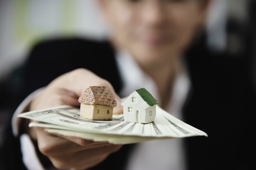 A person holding dollar banknotes with small houses on it 