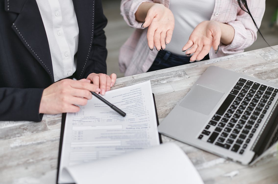 A closeup of two women with a loan requirement document and a laptop