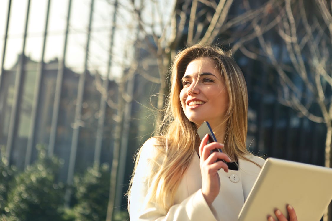 Businesswoman with phone and tablet outdoors.