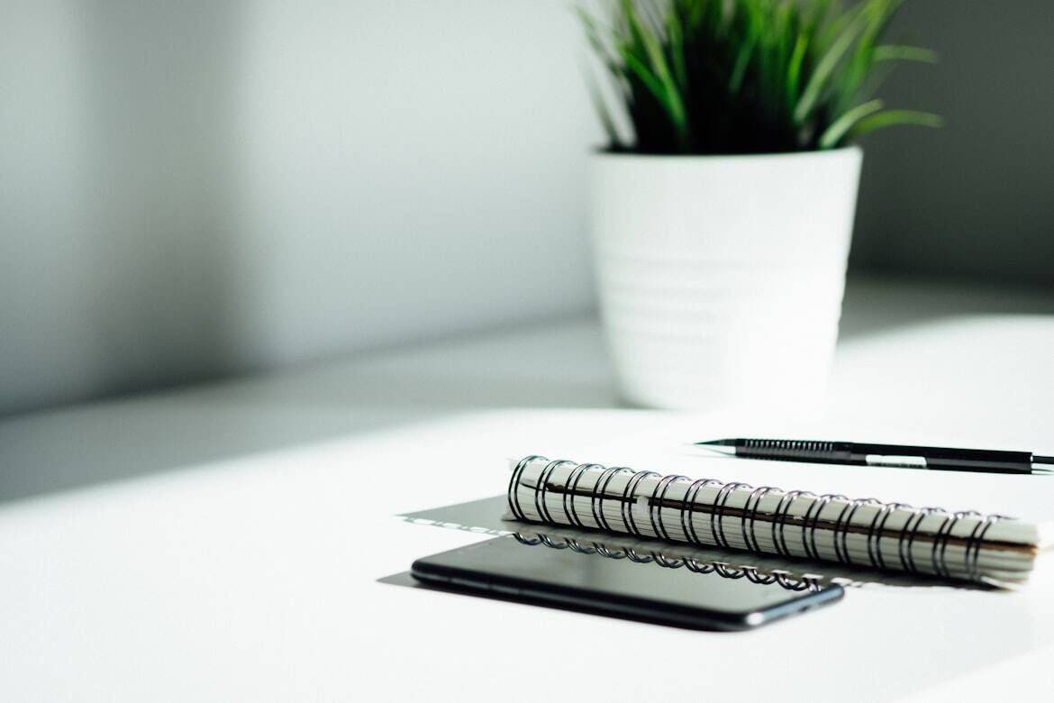 A Notebook, Pen, and Phone Beside a Potted Plant