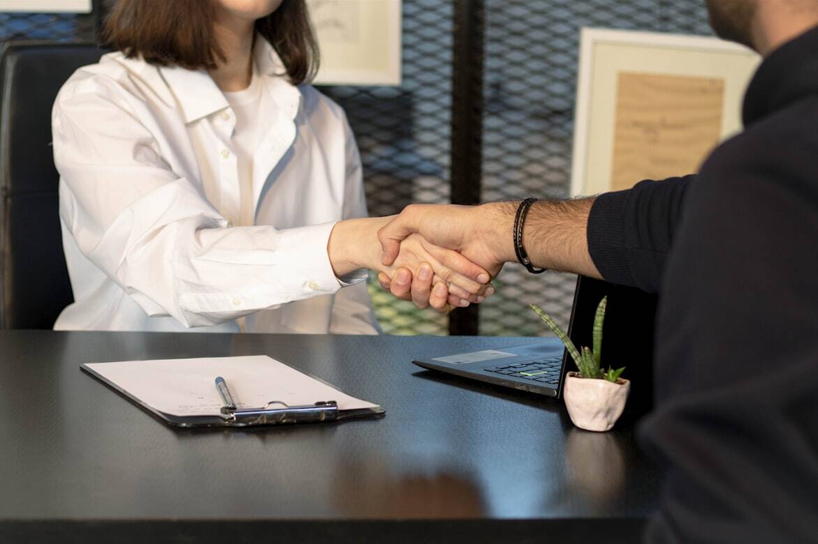 Two individuals shaking hands across a table.